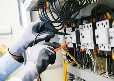 a pair of hands in safety gloves working on an electrical circuit